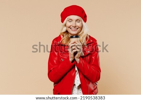 Fun elderly gray-haired blonde woman lady 40s years old wears red beret jacket dress hold takeaway delivery craft paper brown cup coffee to go isolated on plain pastel beige background studio portrait