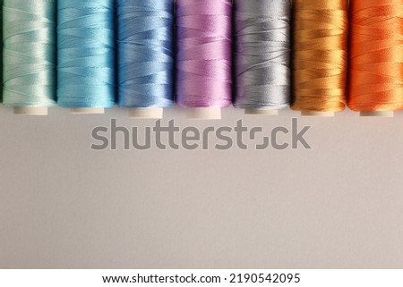 Different colorful sewing threads on light grey background, flat lay. Space for text