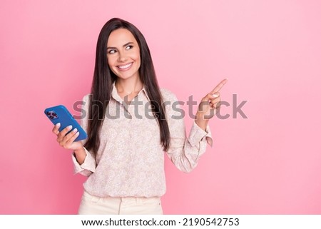 Photo portrait of confident young woman hold device point empty space wear stylish formalwear garment isolated on pink color background