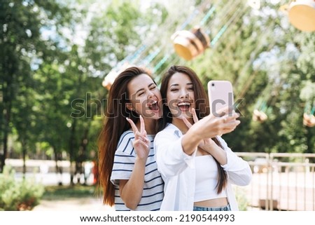 Young women with long hair friends having fun taking selfie on mobile phone at amusement park