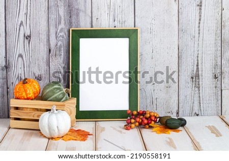 Portrait frame against a light wall with fallen leaves. Frame with pumpkins and space for text. Autumn and Halloween concept.