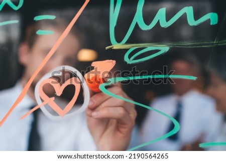 Anonymous blurred male in formal outfit drawing bright signs with colorful marker on glass of transparent window in selective focus