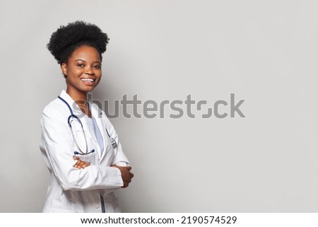 Happy beautiful female doctor in medical coat standing with crossed arms on white banner background