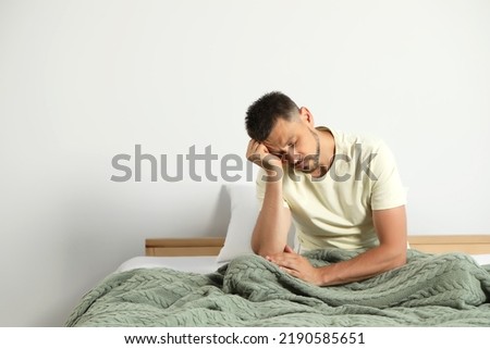 Sleep deprived man sitting on bed at home. Space for text Royalty-Free Stock Photo #2190585651