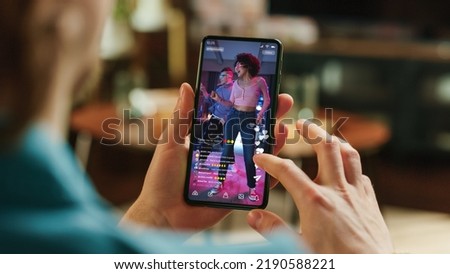 Man Scrolling Feed of Social Media Application and on Display on Smartphone. Male Resting at Home, Checking Social Network on Mobile Device. Close Up Over the Shoulder Photo. Royalty-Free Stock Photo #2190588221
