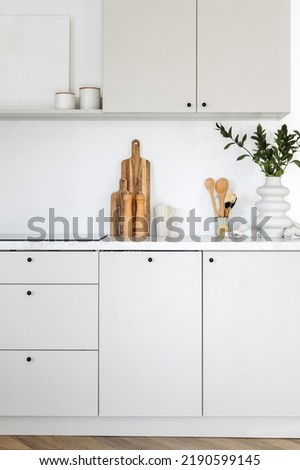 Vertical shot of apartment interior with white kitchen cabinet and cupboards for storing equipment. Tabletop with wooden cutting boards, home decor and kitchenware close to built in induction stove