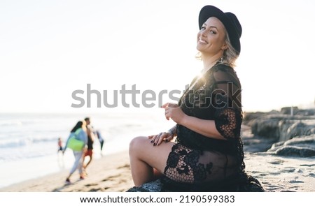 Portrait of girl 20 years old recreating at beach and smiling at camera during summer sunbathing, cheerful tourist in black swimwear posing during bikini season for tanning plus size body and skin