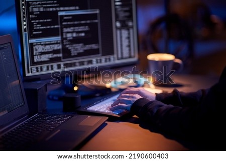 cybercrime, hacking and technology concept - close up of hacker in dark room writing code or using computer virus program for cyber attack Royalty-Free Stock Photo #2190600403