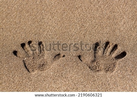 Human handprint on sand at the sandy beach. Palm print. Closeup shot of handprints in the sand as nice nature summer background. Two hand prints on beige sea sand texture. Top view with copy space