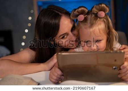 Photo of happy mother and daughter at home. Mom and daughter are watching funny cartoons on tablet computer in the evening. chatting online making video call