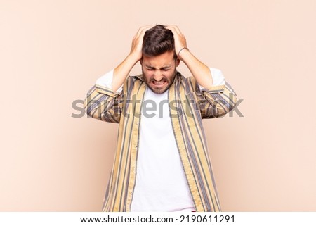 young man feeling stressed and frustrated, raising hands to head, feeling tired, unhappy and with migraine