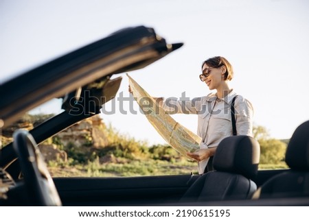 Woman road tripping by cabriolet and looking at the map