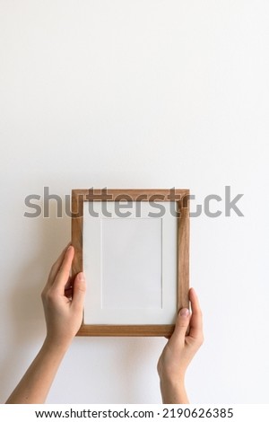 Woman's hands holding a wooden blank picture frame mock up against a white wall. Minimalistic design, display for an image	