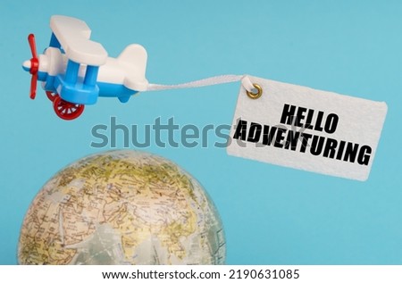 Travel and business concept. On a blue background, a globe and an airplane with a sign - Hello adventuring. Globe out of focus.