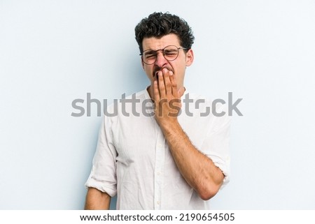 Young caucasian man isolated on blue background yawning showing a tired gesture covering mouth with hand.