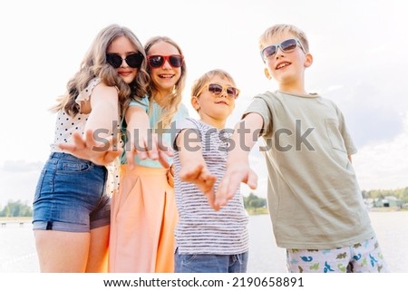 Four children different age in eyeglasses giving high five at camera in the beach outdoor. Teenager girls with two boys brother at summer camp together. Vacation, relax, active lifestyle concept.