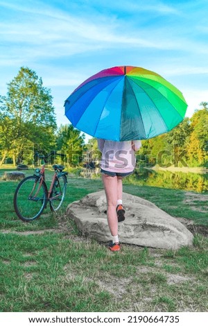 girl on the river bank with a large six-color rainbow umbrella on a summer morning.