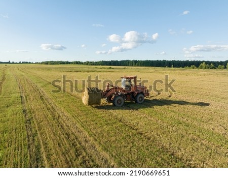 Hay Making. Front end loader loads round bales of straw from Hay Trailer. Storage hay at farm. Hay rolls as Forage feed for livestock. Winter Wheat planting, autumn grain harvest, drone view.  Royalty-Free Stock Photo #2190669651