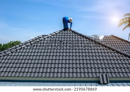 Roof repair, worker replacing gray tiles or shingles on house with blue sky as background and copy space, Roofing - construction worker standing on a roof covering it with tiles. Royalty-Free Stock Photo #2190678869