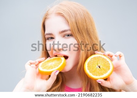 Funny smiling young woman eating juicy halves of oranges isolated on gray background. Healthy eating concept. Diet.	