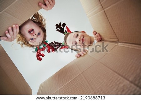 Smiling sibling child girl and boy open Christmas gift and look inside in cardboard box. View from box. Funny Christmas time and holidays.