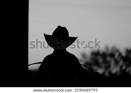 Young cowboy on ranch in silhouette black and white, western rodeo industry concept.