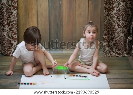 Little children paint on a large sheet of paper on the floor
