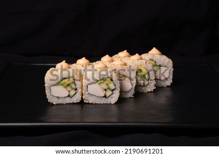 California sushi roll covered with drops of sauce on black surface