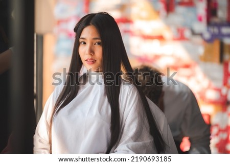 Young beautiful and smiling woman sitting in salon chair with cloth wrapped around getting hair cut and hair styling done in modern salon by experienced male professional barber