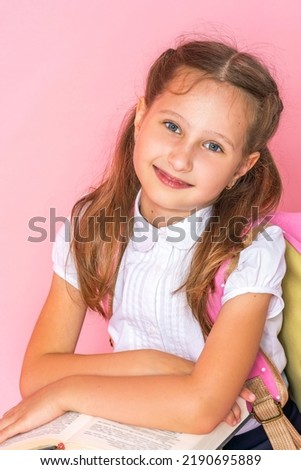 happy smiling little girl in uniform with a backpack and books poses on pink background in studio. schoolgirl rejoices at beginning of classes, goes to study with pleasure. Back to school. Close up
