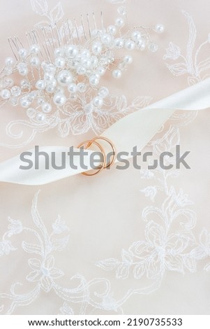 Gold rings and hairpin for the bride's hair on white lace. Wedding vertical card. Copy space, selective focus