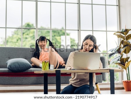 Asian woman mother relaxing using laptop computer working and video conference meeting chat with girl daughter play on sofa at home.work from home