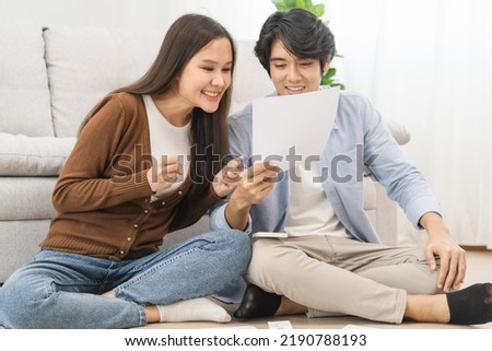 Happy excited, smiling asian young couple love, wife and husband hold paper letter, reading paperwork document getting, receive job promotion, tax refund or loan mortgage approval, good news by mail. Royalty-Free Stock Photo #2190788193
