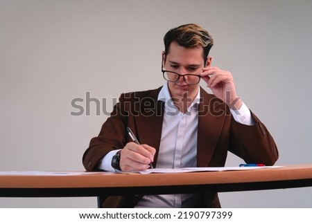 Business man working at a desk. Business executive dressed in brown suit, glasses and white shirt. Man of business working with a white background behind. High quality photo