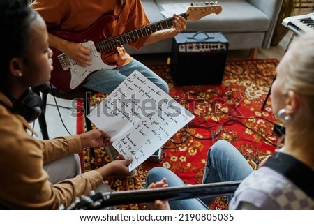 Close up of black young woman writing songs with music band and holding lyrics sheet, copy space Royalty-Free Stock Photo #2190805035