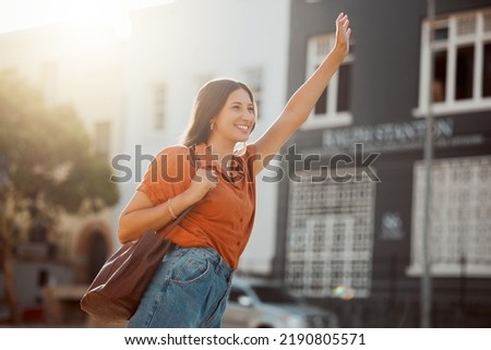 Waving for a taxi, waiting in the street for a ride outside. Smiling urban woman wants to travel downtown for work or fun with a cab. Lady gestures for transportation with confident arm raised. Royalty-Free Stock Photo #2190805571
