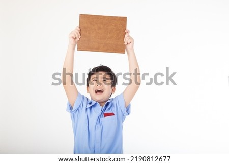 Portrait of a little young handsome Asian kid boy student in school uniform, holding a blank board with copy space, isolated on white background. Concept of happy education.