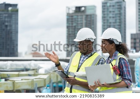 Group of African American engineer working in sewer pipes area at construction site. Male engineer and woman engineer discussing for maintenance sewer pipes, water tank on rooftop of building Royalty-Free Stock Photo #2190835389