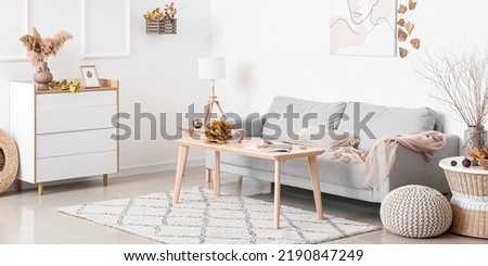 Interior of light living room with grey sofa, table and autumn decor