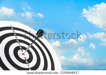 Dartboard with hit bullseye against blue cloudy sky, closeup
