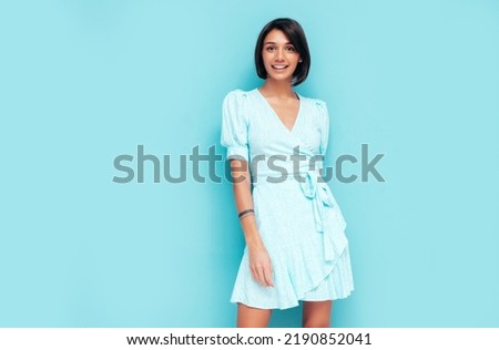 Portrait of young beautiful smiling female in trendy summer dress. Carefree woman posing near blue wall in studio. Positive model having fun indoors. Cheerful and happy. Isolated Royalty-Free Stock Photo #2190852041