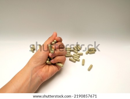 Supplements, vitamins, or pills for health care and treatment. Andrographis paniculata capsules. A hand is gripping green pills.
