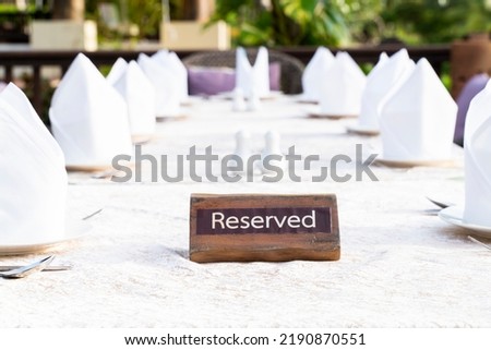 A wooden reserved signage is set on the formal dining table with neatly white napkin folded in the outdoor atmosphere.