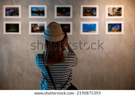 Photographer visit at photo frame to leaning against at show exhibit artwork gallery, Asian woman takes picture art gallery collection in front framed paintings pictures on white wall with camera Royalty-Free Stock Photo #2190875393