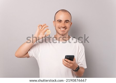 A picture of a man holding a bitcoin and his phone while he smles because of his succes