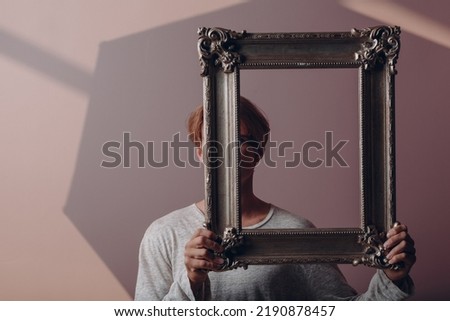 Millenial young man close face with gilded picture frame portrait.