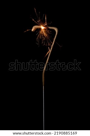 Burning golden sparkler in shape of number seven, digit 7, isolated on black background