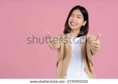 Young smiling fun happy woman of asian showing thumb up like gesture blink isolated on pink background studio portrait. People lifestyle concept