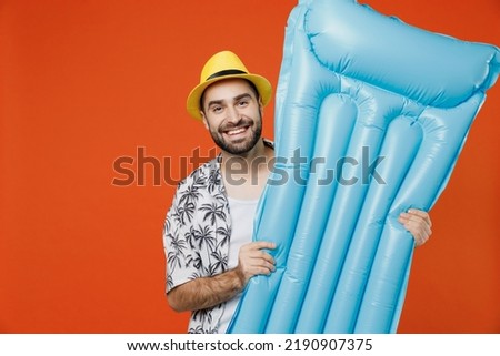 Young tourist man wear beach shirt hat hold inflatable mattress near hotel pool travel abroad on weekends isolated on plain orange background studio portrait. Summer vacation sea rest sun tan concept