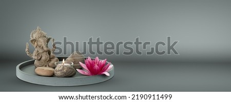 beautiful home decoration with ganesha statue, candlelight and pink lotus blossom, floral purity on matt grey background with copy space